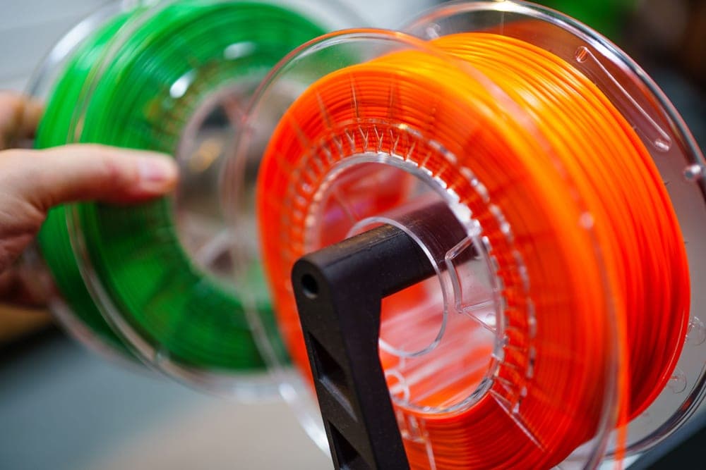 Spools of different colored filament beside a 3D printer